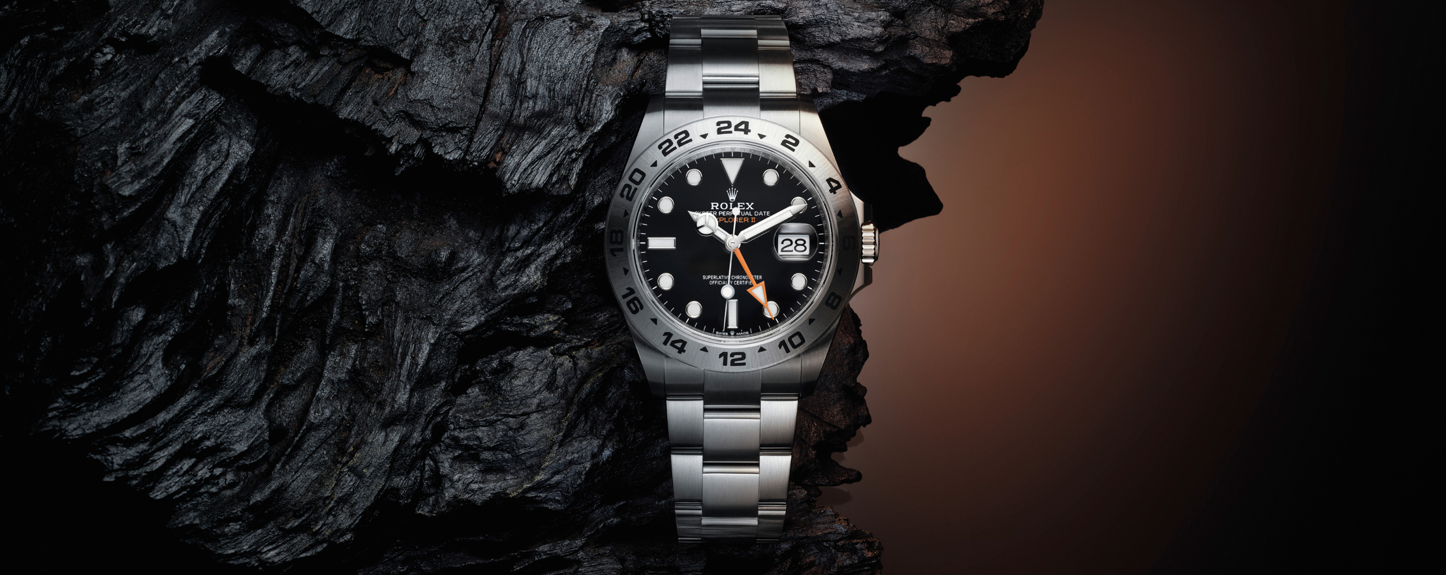 A silver wristwatch with a black bezel and dial, featuring white markers and text. The watch is positioned vertically against a gradient background.