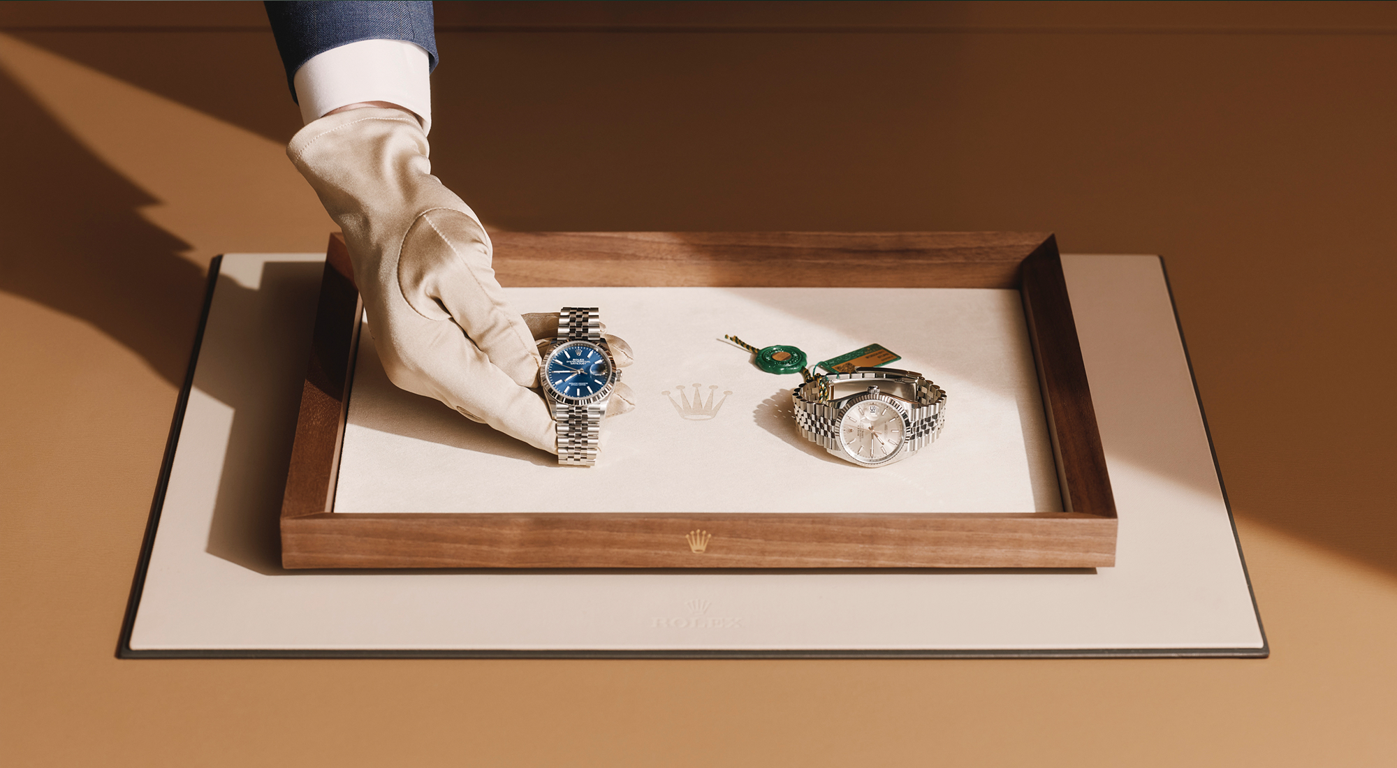 Gloved hands holding a wristwatch with a green and gold Superlative Chronometer certification tag attached to the metal bracelet.